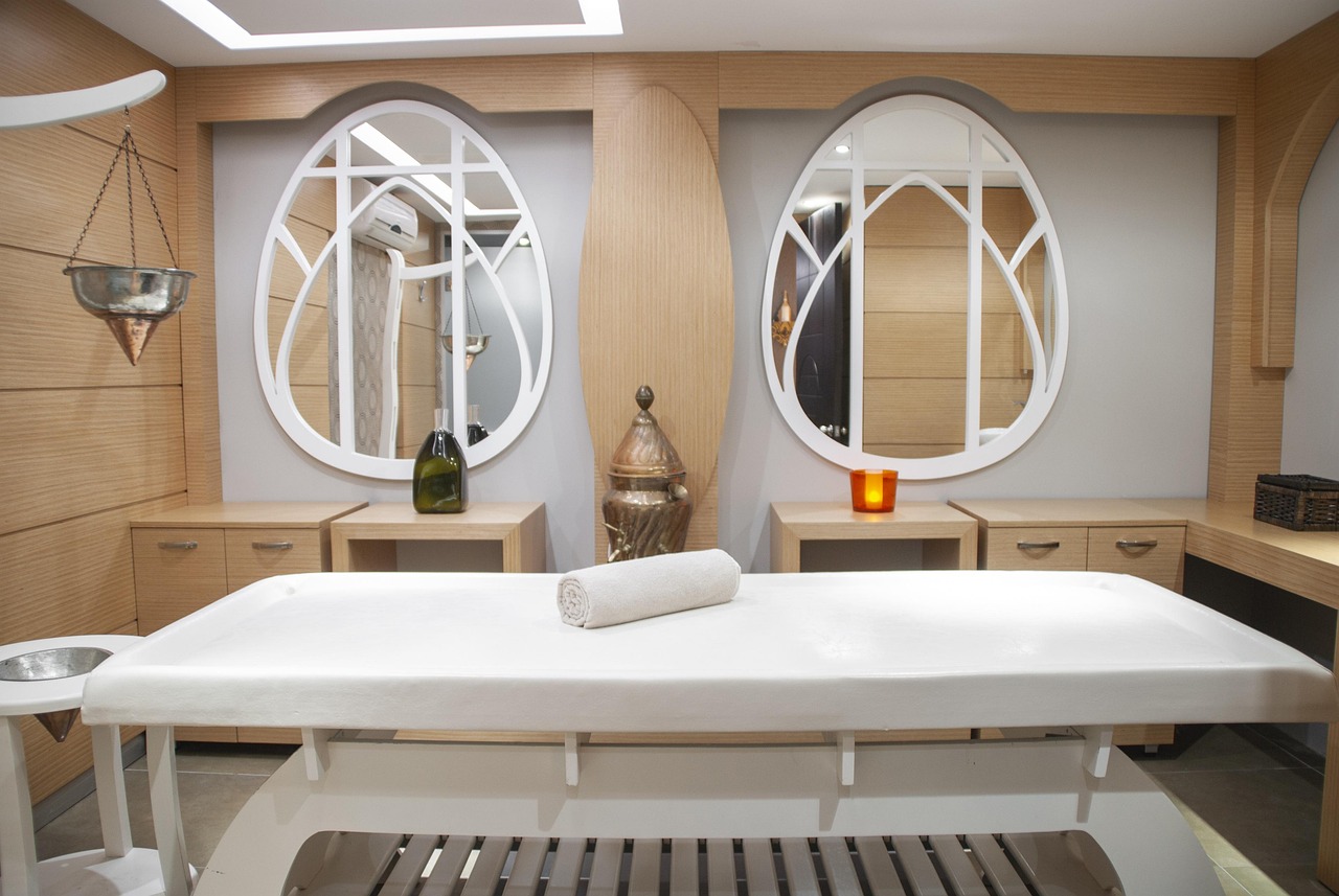 The Loom treatment room: a made-up massage table with warm low light, folded linen, and a plant in the corner